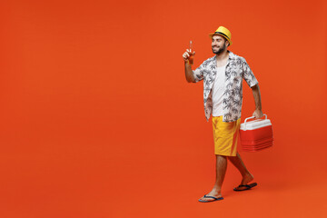 Young side view happy cool tourist man 20s in beach shirt hat hold beer bottle alcohol cooler box fridge isolated on plain orange background studio portrait. Summer vacation sea rest sun tan concept.