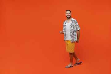Fototapeta premium Full body young smiling happy fun cool tourist man wear beach shirt walking going strolling look camera isolated on plain orange background studio portrait. Summer vacation sea rest sun tan concept.