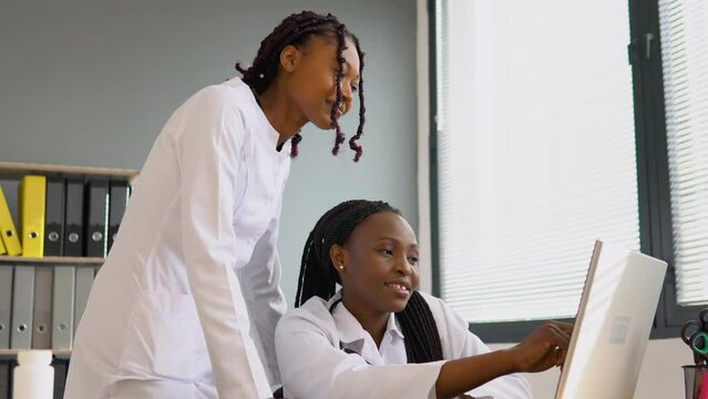 Two african women students discussing patient treatment plan showing something on laptop. Online treatment