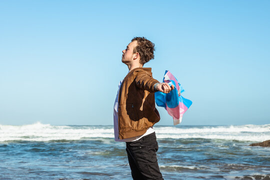 Man with colorful transgender flag near sea