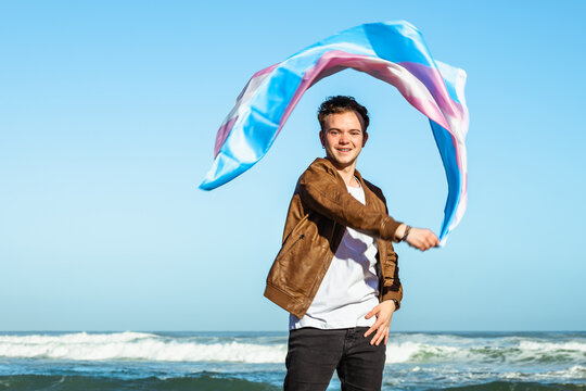 Content man with colorful transgender flag near sea