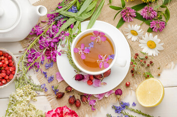 Herbal tea with rosehip, chamomile and lemon in a white cup on a white wooden table with flowers