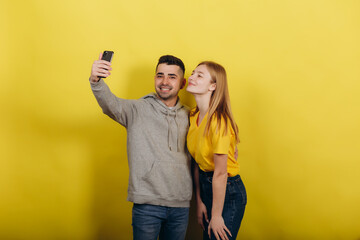 Photo of happy excited young loving couple standing isolated over yellow wall background take a selfie by mobile phone.