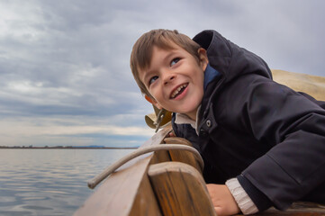 retrato de niño sonriendo , asomándose al borde del barco para mirar al agua, durante un paseo barca por la albufera de Valencia, con un cielo nublado.