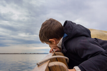 niño asomándose al borde del barco para mirar al agua, durante un paseo por la laguna de Valencia, con un cielo nublado.