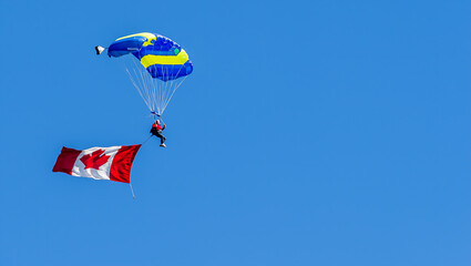 Sky diving parachutist with a Canadian flag, decending against a blue sky