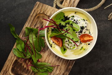 Mashed potatoes with fish in cream sauce, tomatoes and beetroot leaves in paper container on wood board isolated on dark background. Healthy food delivery service and daily ration concept.