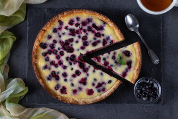 Homemade open blackcurrant shortbread pie on a slate plate on a dark background, top view