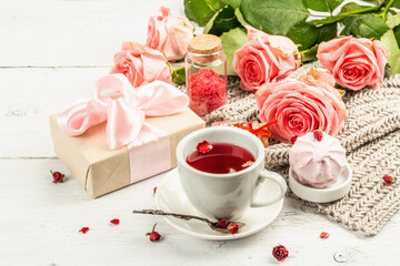 The concept of romantic tea. Wrapped gift, hibiscus tea, a bouquet of delicate roses, sweets