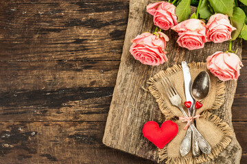 Rustic table setting for romantic dinner. Bouquet of fresh roses, cutlery and heart