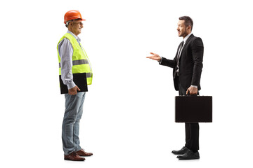 Full length profile shot of a businessman talking to a male engineer with a safety vest and hardhat