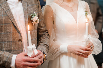 The bride and groom hold shining candles during the ceremony in the church. Hands of newlyweds with candles in the church. Church religious details. Traditions