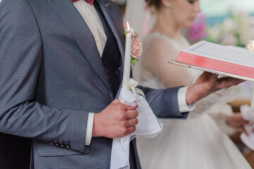 The bride and groom hold shining candles during the ceremony in the church. Hands of newlyweds with candles in the church. Church religious details. Traditions