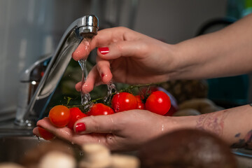 Close up female's hands washing homegrown organic red cherry tomatoes with the tap water.