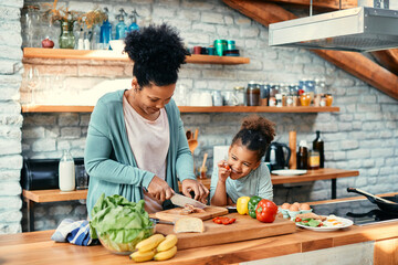 Happy black mother and daughter have fun while preparing food in the kitchen.