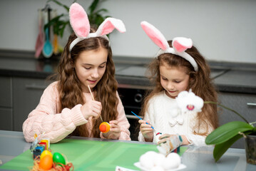 Two girls in hare ears paint eggs. Easter. They are at home in the kitchen. Preparation for the holiday.