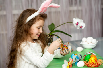 Fototapeta na wymiar A girls in hare ears paints eggs. Easter. She is at home in the kitchen. Preparation for the holiday.