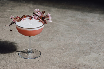 cherry blossom gin cocktail with egg white on concrete in the sunlight