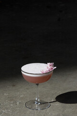 cherry blossom gin cocktail with egg white on concrete in the sunlight