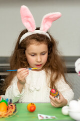 A girls in hare ears paints eggs. Easter. She is at home in the kitchen. Preparation for the holiday.