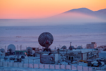Large satellite dishes on the background of snow-covered tundra and mountains at sunset....