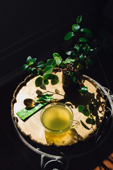 Green matcha tea in glass cup on brass tray with indoor plants and gold spoon