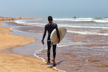 Unknown man in a wetsuit walking holding a surfboard in his hands along the Atlantic coast....