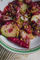 radicchio salad with watermelon radish, blood orange, pistachios on white plate with green greek key
