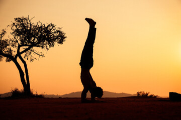 Young man silhouette doing yoga at the sunset on a top of the mountain with the sun behind