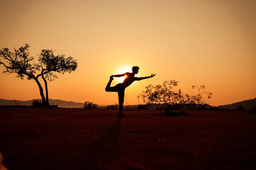 Young man silhouette doing yoga at the sunset on a top of the mountain with the sun behind