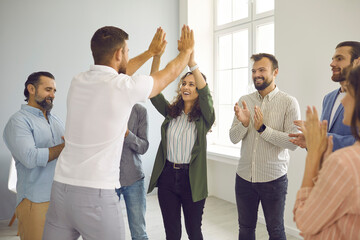 Successful man and woman give each other five when meeting colleagues in bright, spacious office. Group of happy people applaud congratulating their employees. Concept of business and team success.
