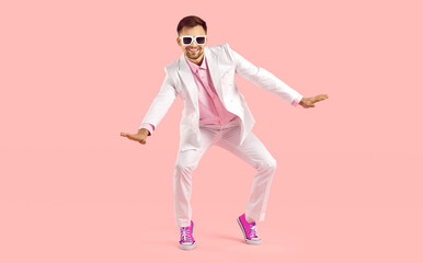 Happy millennial guy in suit and pink converse dance on pink studio background. Smiling stylish young Caucasian man in formalwear and tennis shoes make moves have fun. Fashion and style. - obrazy, fototapety, plakaty