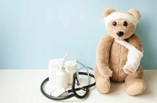 A teddy bear with a broken arm and a sore head sits on a blue background, there is medicine nearby and a fanidoscope lies.  The concept of children's medicine.  Banner place for copy text.