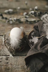 Rustic Easter still life. Natural egg in nest with feathers, vintage plate, pussy willow branches and napkin on aged wood. Easter table decoration