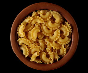 Pasta cornetti creste macaroni pile in clay pot isolated on black, top view