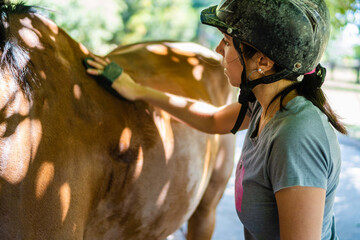 young latina woman rider combing her horse in a barn