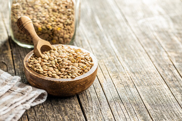 Uncooked brown lentils. Raw legume in bowl on wooden table.