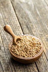 Uncooked brown lentils. Raw legume in bowl on wooden table.