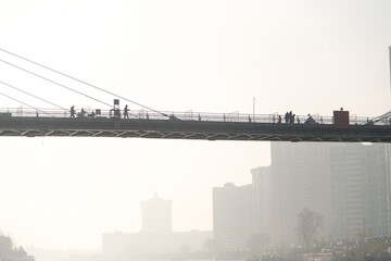 bridge over the river in the fog. People walk on a suspension bridge