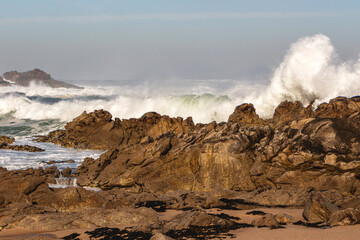 Picturesque coastline of the Atlantic Ocean with breaking waves against old big brown rocks with high splashes of blue water with white foam, Portugal