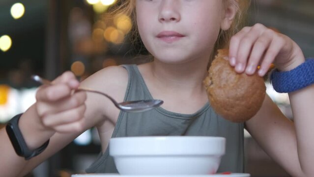 Child girl eating soup and tasty burger in restaurant