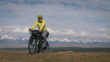 Obraz premium The man travel on mixed terrain cycle touring with bikepacking. The traveler journey with bicycle bags. Sport tourism bikepacking, bike, sportswear in green black colors. Mountain snow capped.