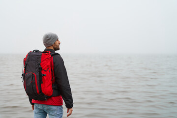 Freedom concept. Young male adventurer with backpack looks at sea on winter morning