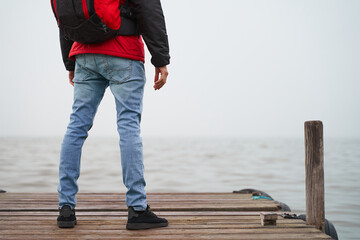 Detail of legs of tourist at wooden dock by nordic sea with mist on winter morning