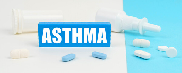 On a white and blue surface are pills, a spray and a wooden sign with the inscription - ASTHMA