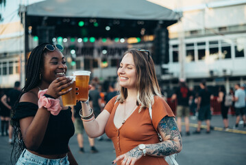 Two beautiful friends drinking beer and having fun at music festival