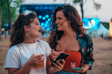 Two beautiful friends using a smartphone on a music festival