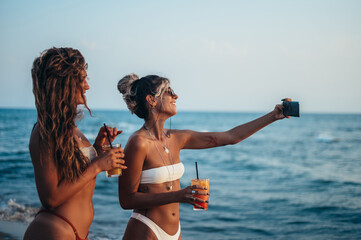 Friends enjoying vacation together and taking selfie on the beach using smartphone