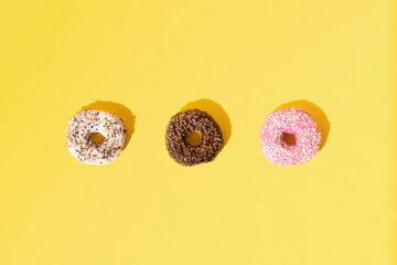 Arranged ring donuts with white, pink and chocolate glaze. Colorful crumbs on a yellow pastel background. Pattern. Copy space. Flat lay.