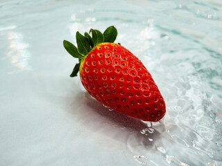 Red strawberry fruit in flowing water on bright background